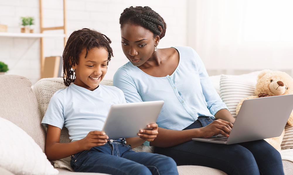 Woman and daughter on couch looking at tablet together.